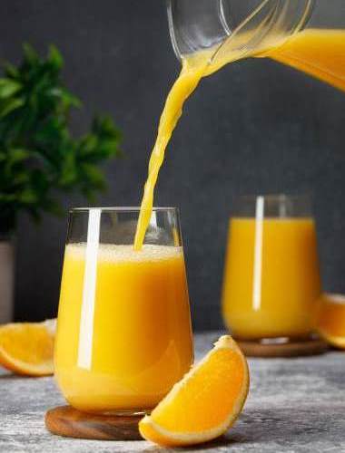 orange juice pouring into glass from jug on table with dark background